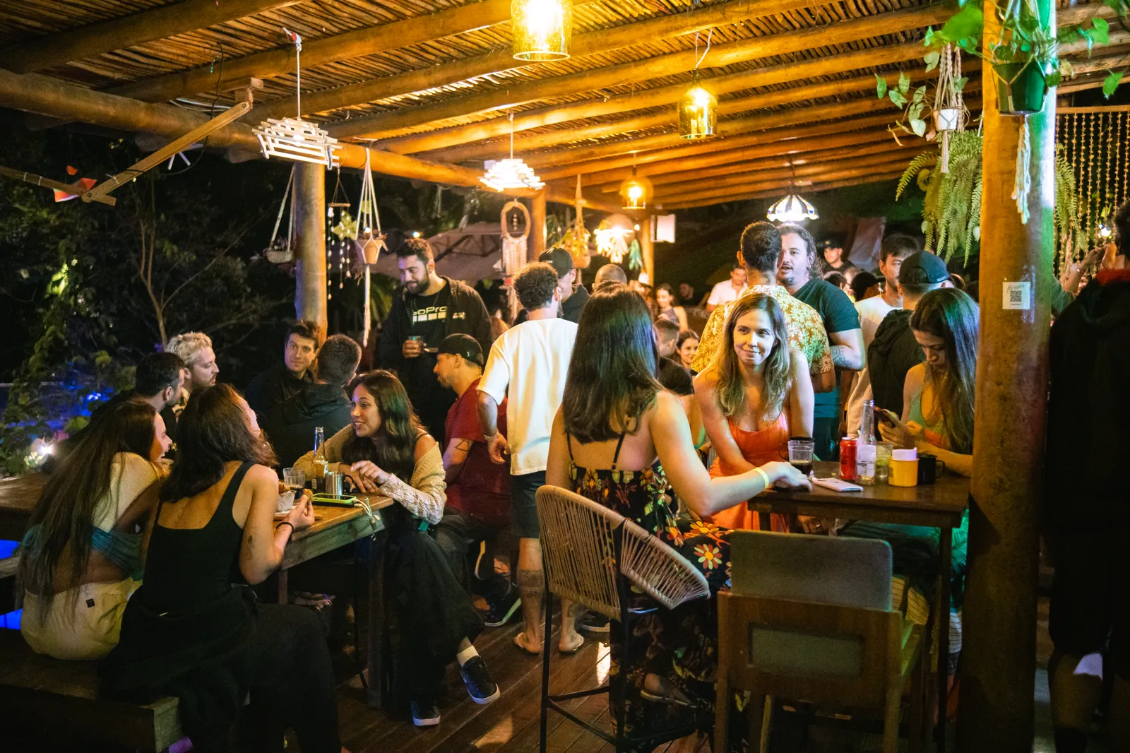 Floresta Bar cheio à noite, com lanternas acesas e mesas de madeira