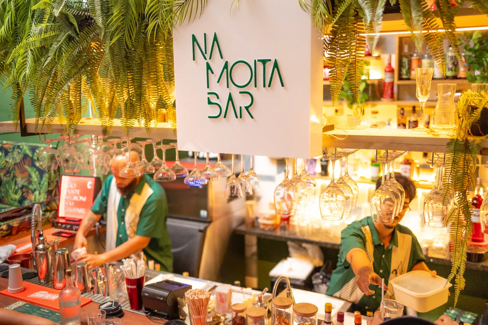 Dois bartenders de verde preparando coquetéis no balcão do Na Moita Bar