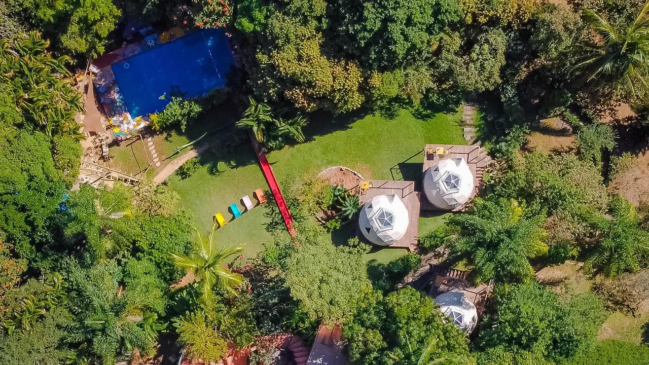 Vista aérea dos 9.000 m² do Hostel da Vila em Ilhabela, com piscina, tobogã e domos em meio à Mata Atlântica