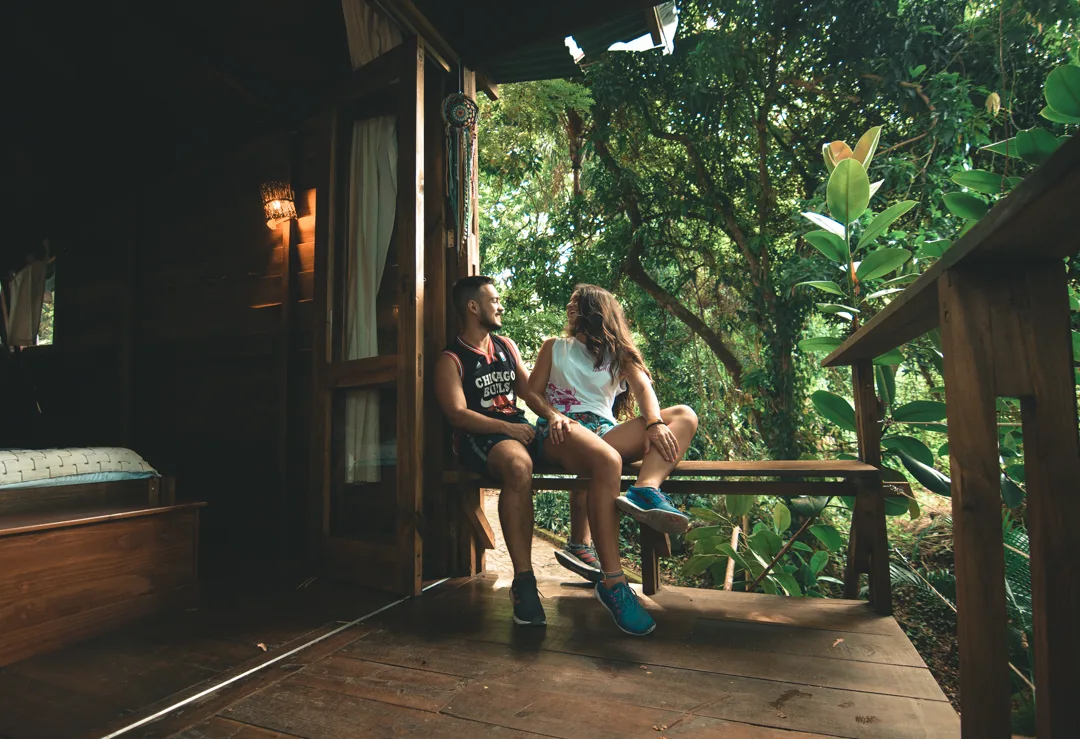 Casal na varanda da casa na árvore do Hostel da Vila em Ilhabela, cercado de natureza