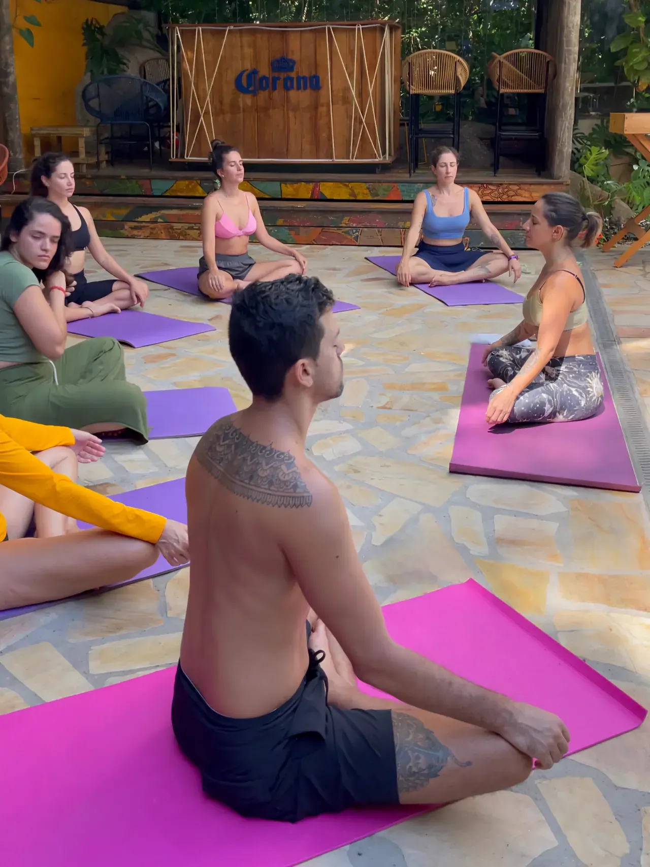 Aula de yoga em círculo no pátio de pedra do Hostel da Vila, com o palco do bar ao fundo