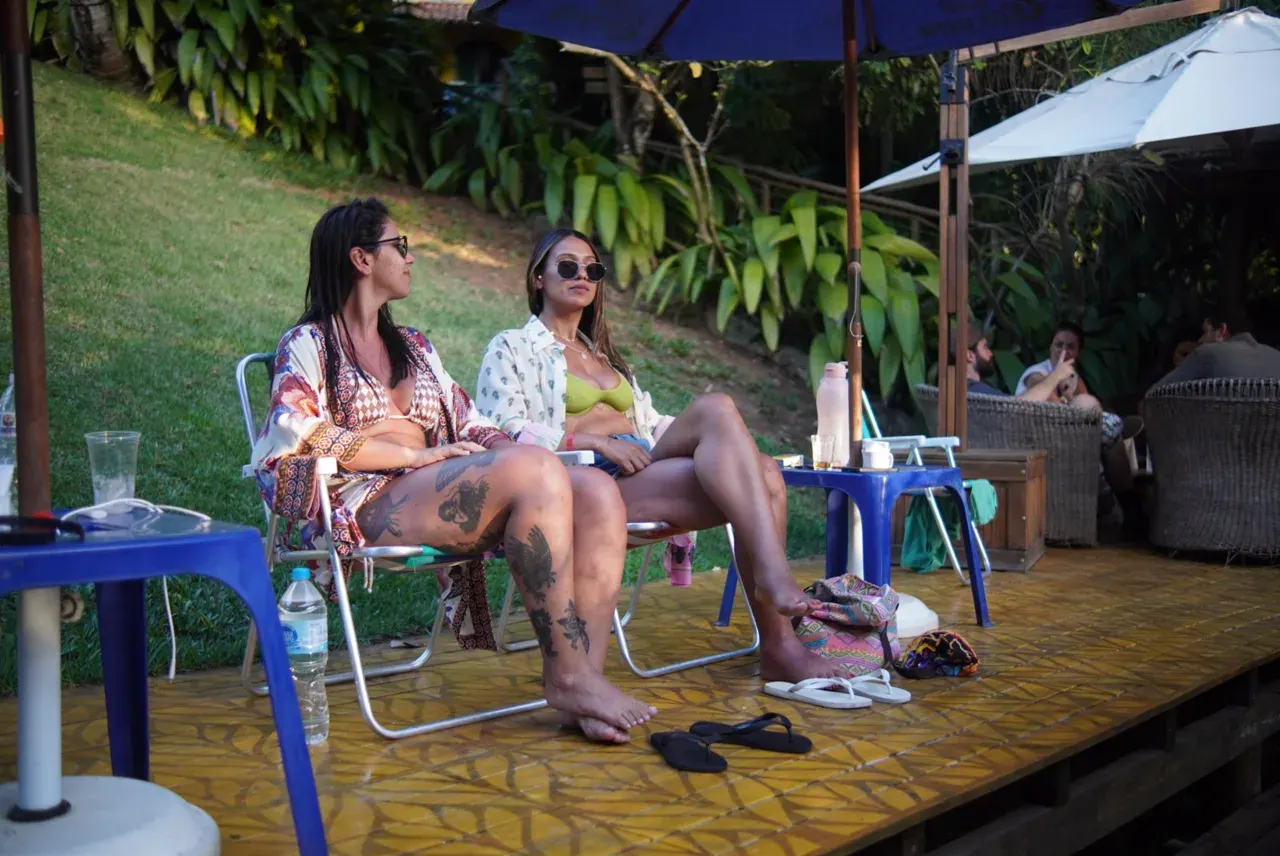 Duas pessoas em cadeiras de sol num deck de madeira, descansando à sombra de guarda-sóis