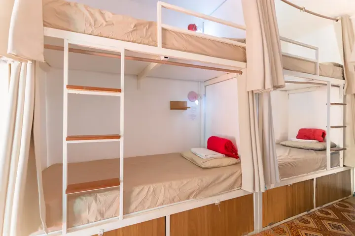Beliches de hostel com cortinas individuais, escada de madeira, prateleira e luz de leitura em cada cama