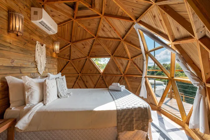 Interior do domo geodésico do Hostel da Vila, com cama de casal e janela triangular aberta para o verde