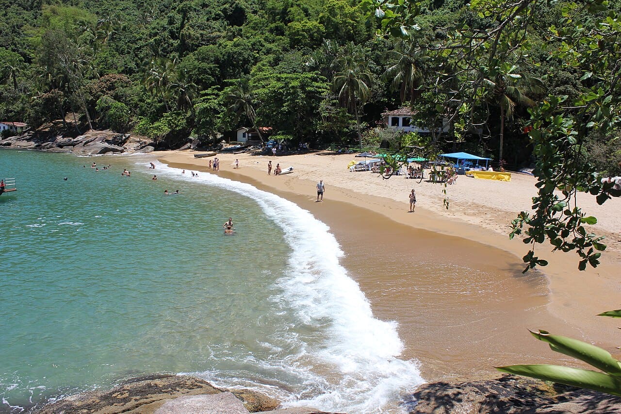 Águas transparentes e areia clara cercadas de mata na Praia da Fome, em Ilhabela