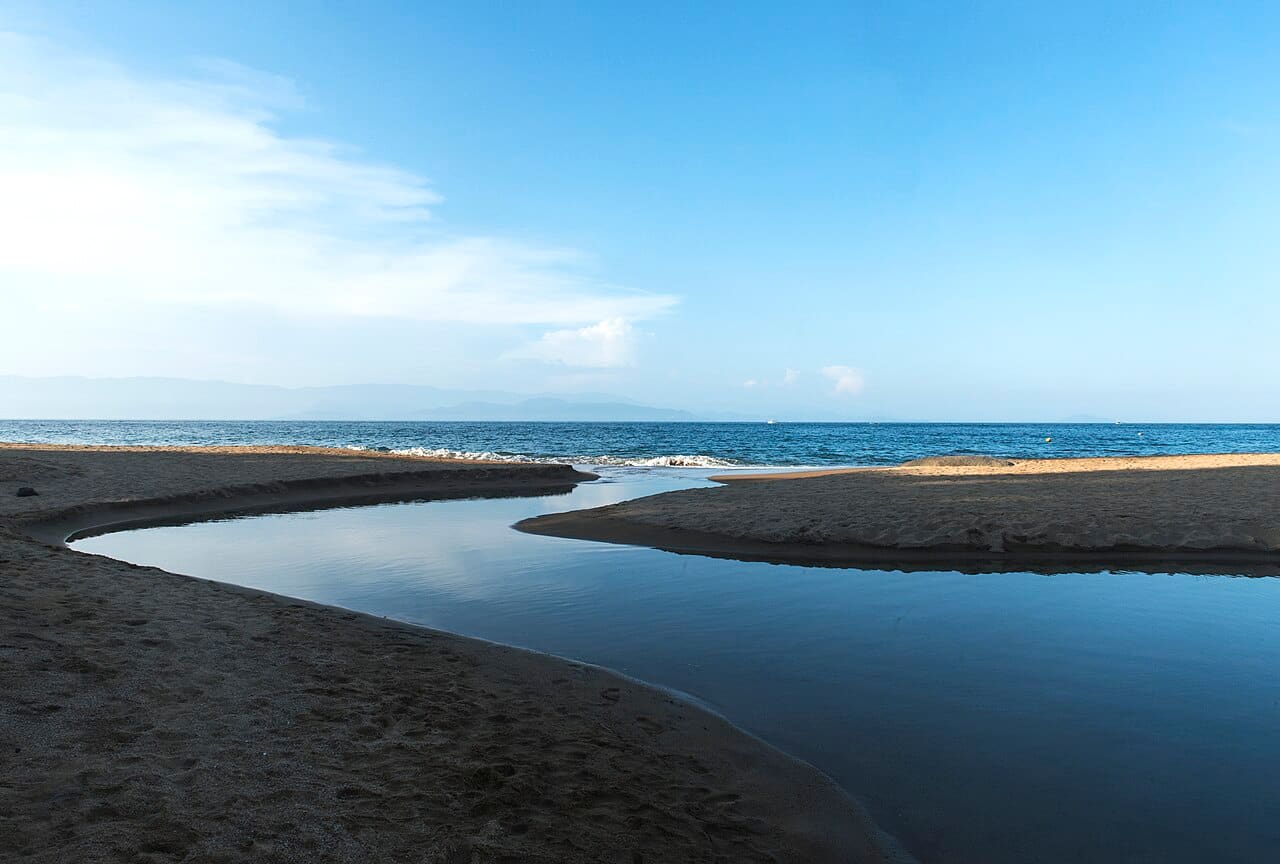 Rio desaguando entre pedras na areia clara da Praia do Jabaquara, em Ilhabela