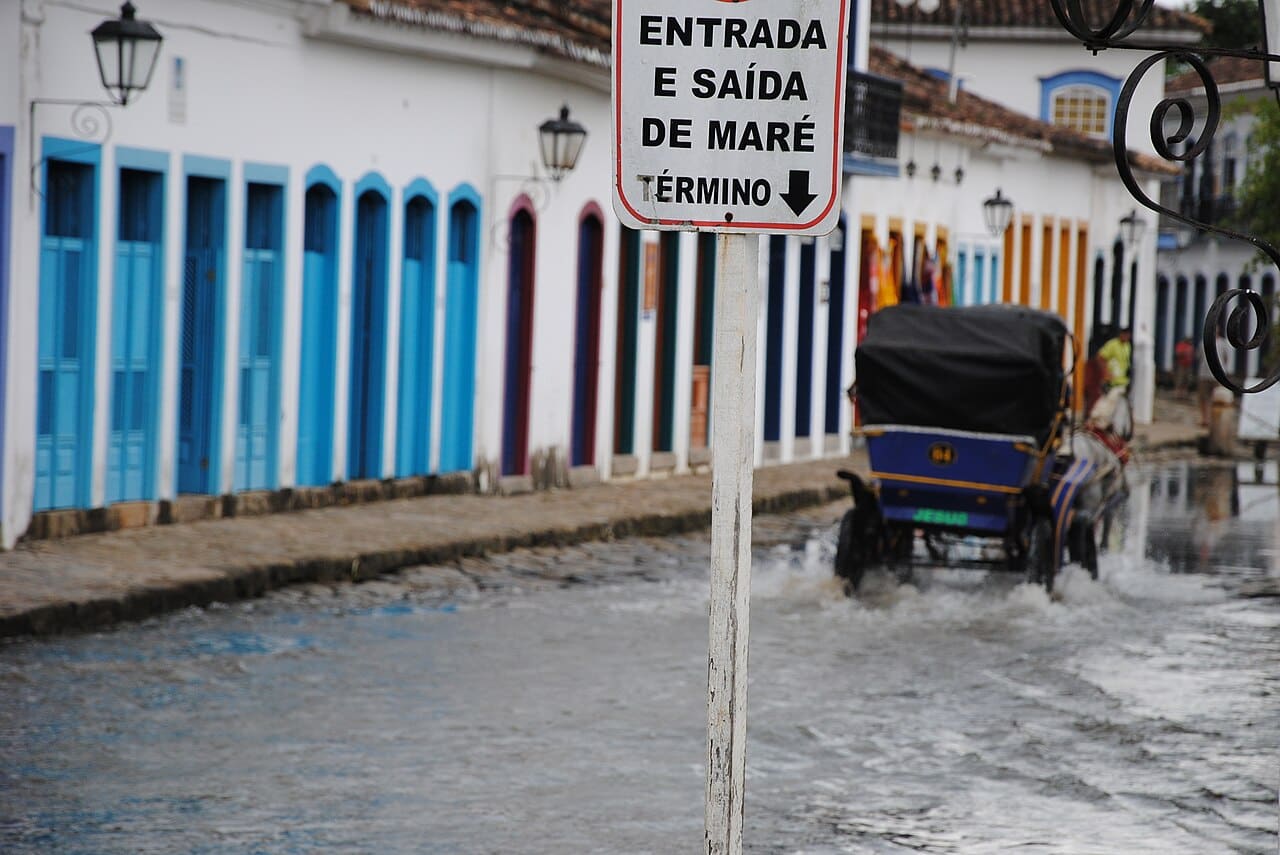 Maré alta invadindo a rua de pedra do centro histórico de Paraty, com casario colonial refletido na água