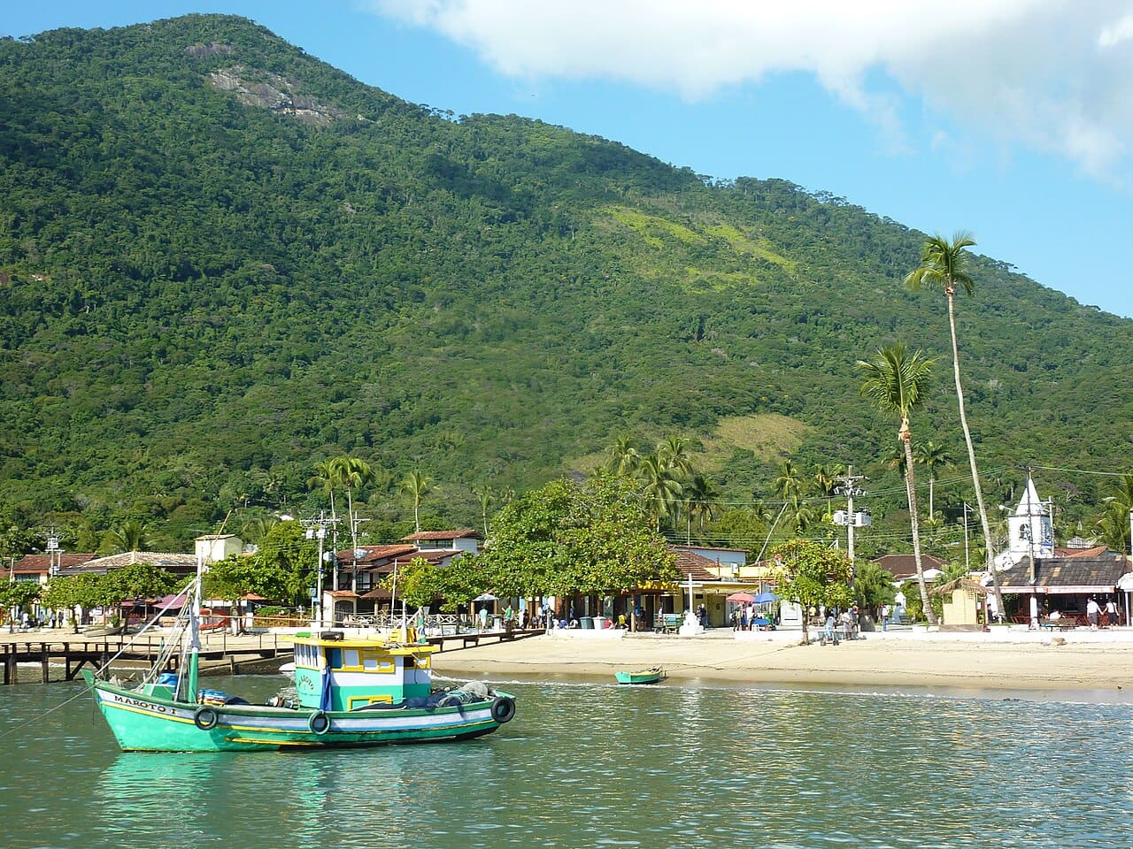 Barco ancorado em frente ao casario da Vila do Abraão, com morros de Mata Atlântica ao fundo